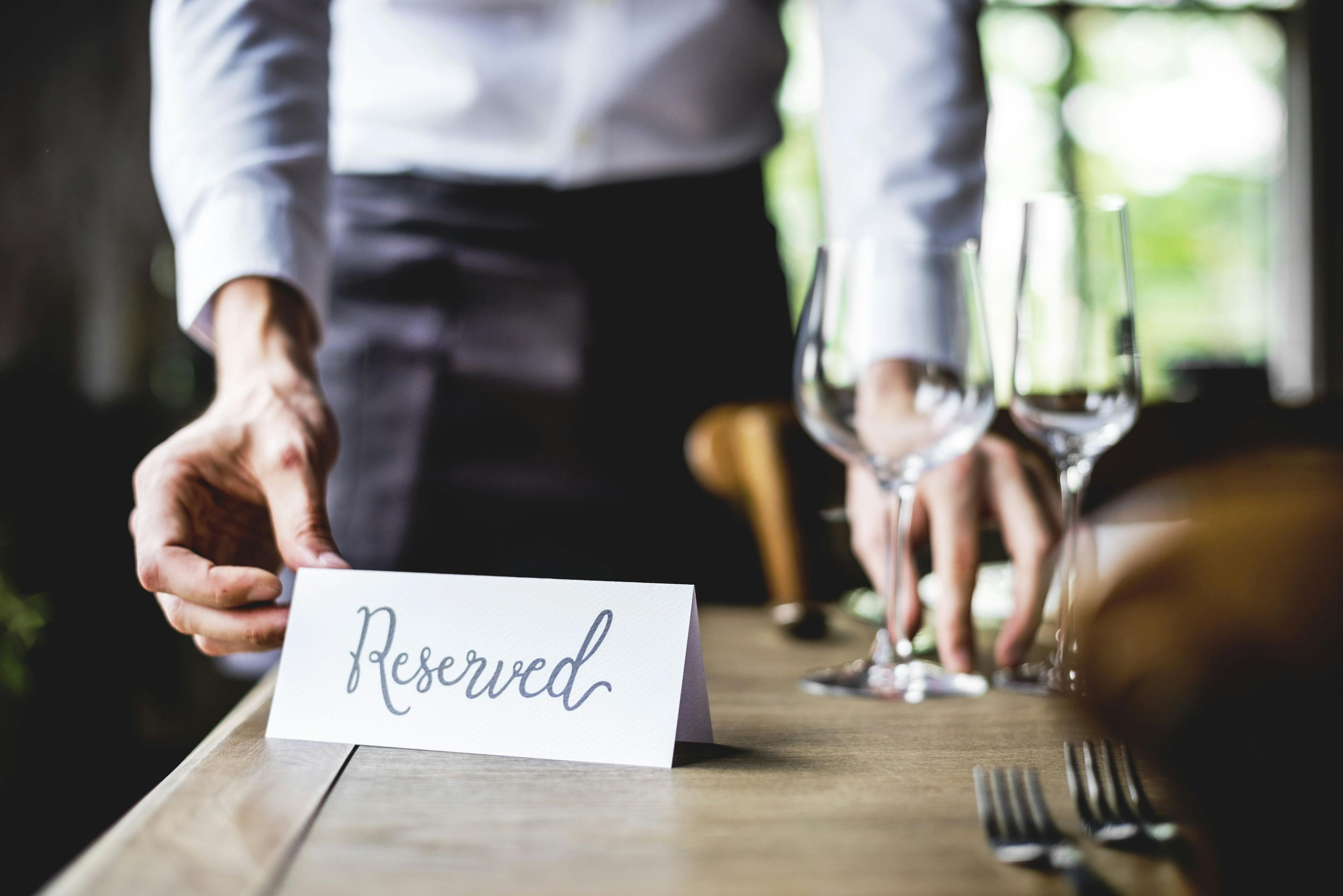 An image of a restaurant waiter placing a reserved sign on a table, indicating that it is reserved for a particular reservation.