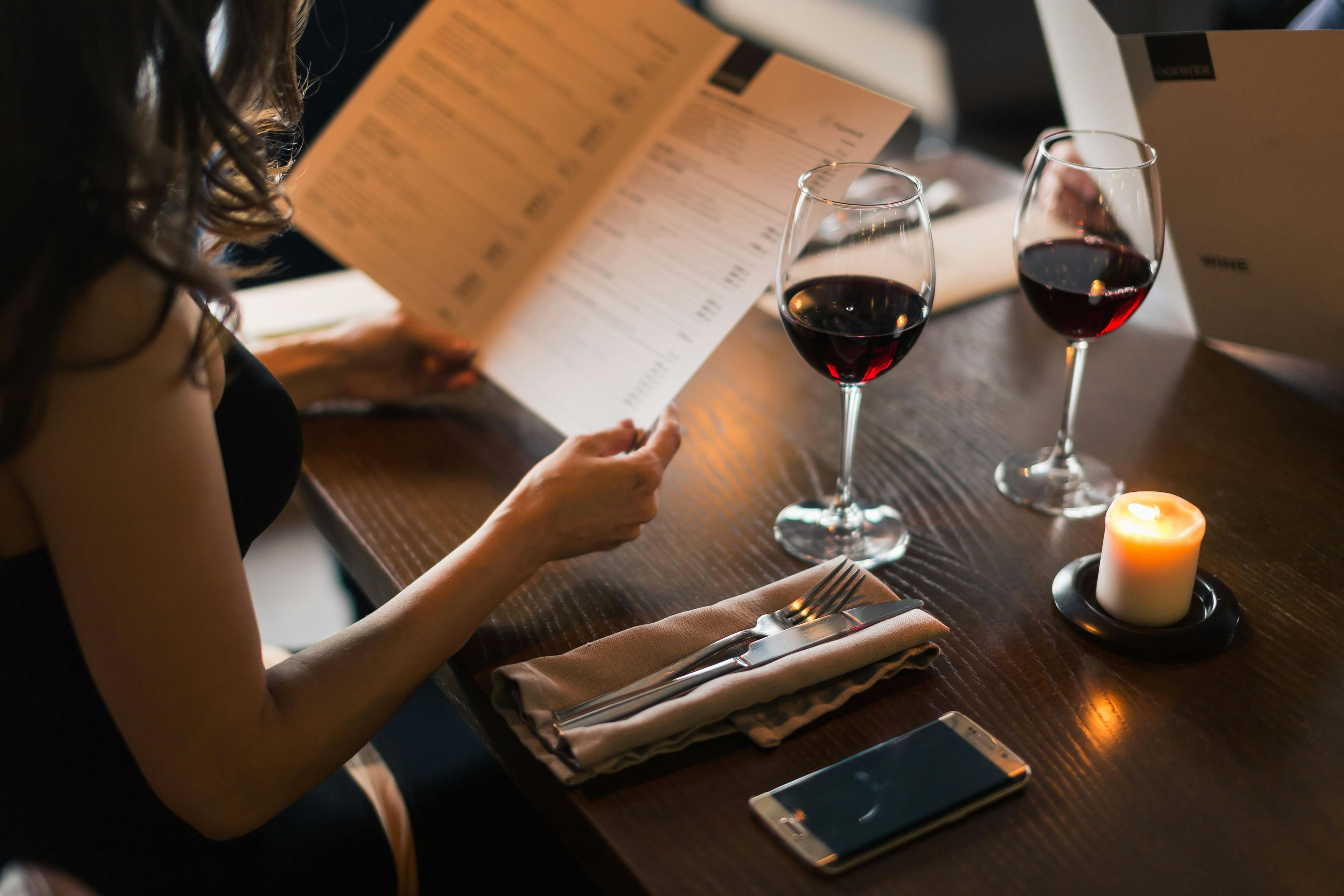 Woman holding a menu and a glass of wine.