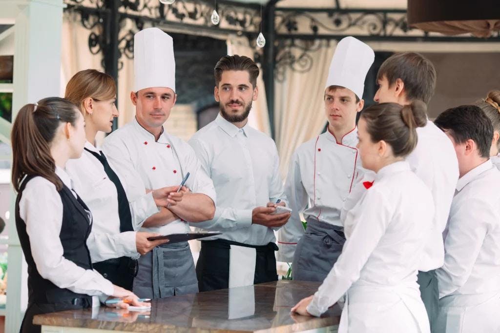 A group of chefs in uniform gathered around a table discussing restaurant reservations.