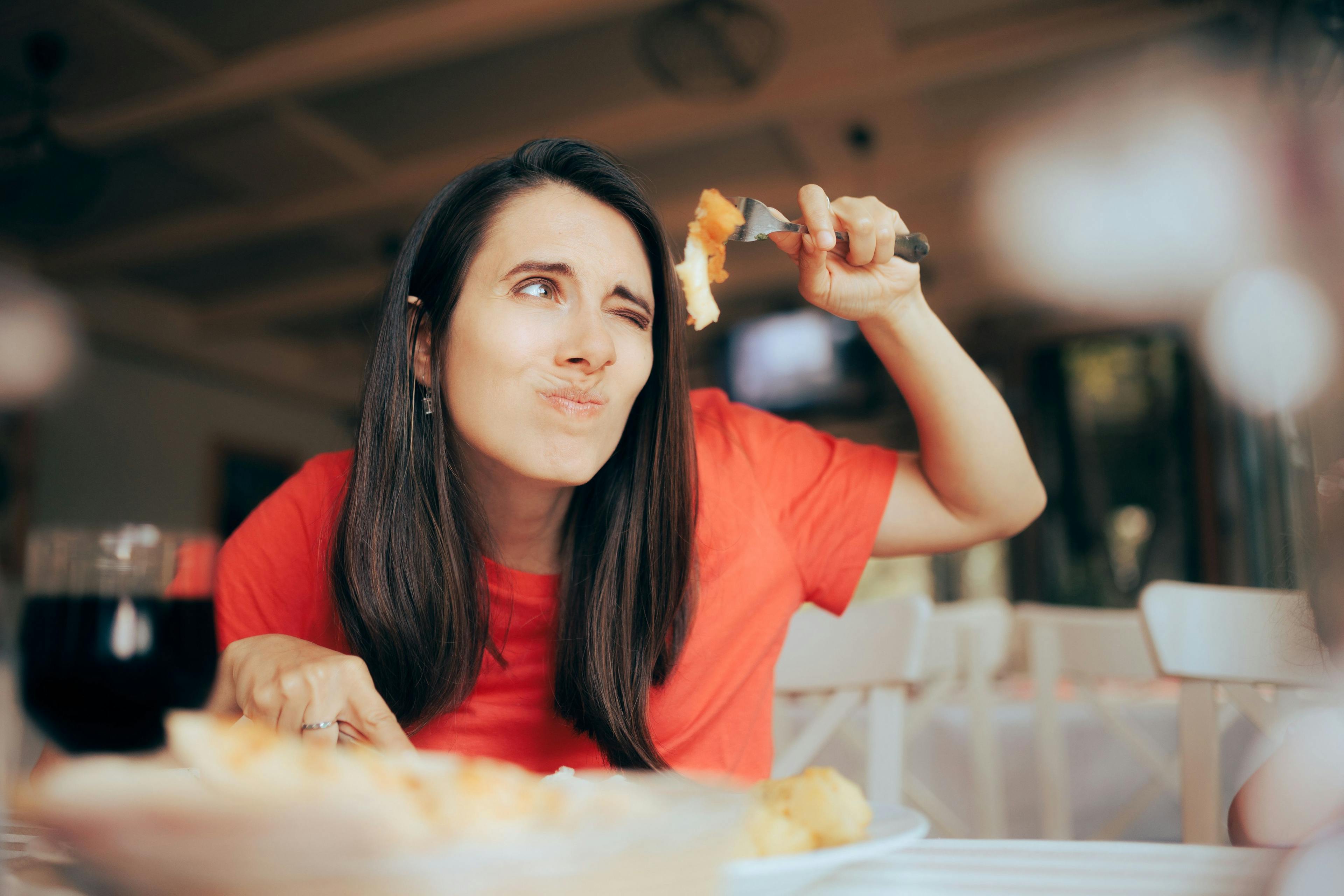 A woman enjoying a slice of pizza, highlighting the importance of displaying food allergies in menus.