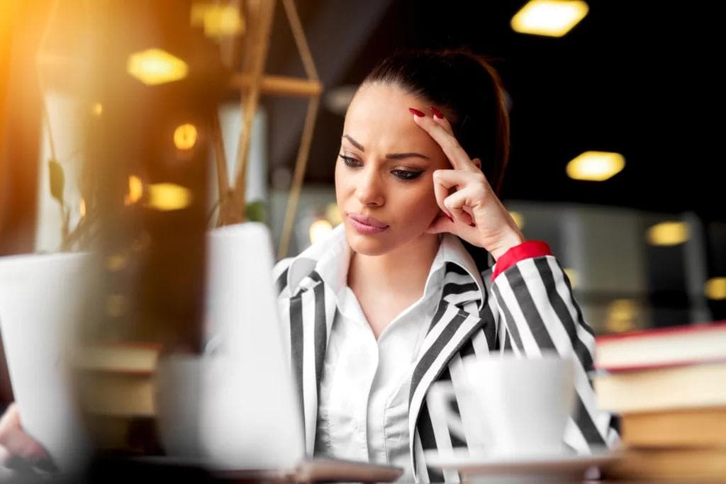 A professional woman in a suit, visibly distressed, rests her head in her hands while seated at a table.