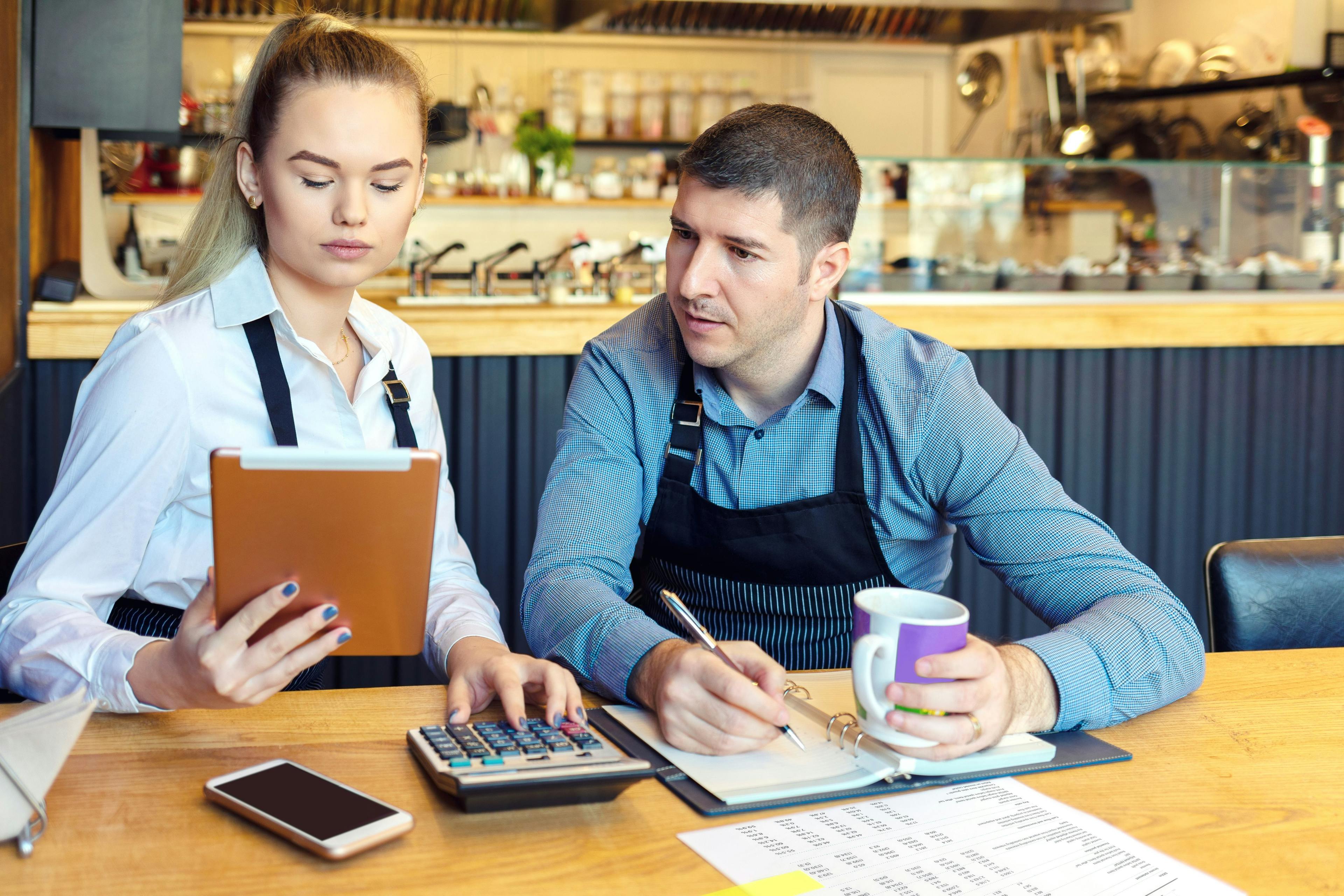 Man and woman using calculator for restaurant revenue management.