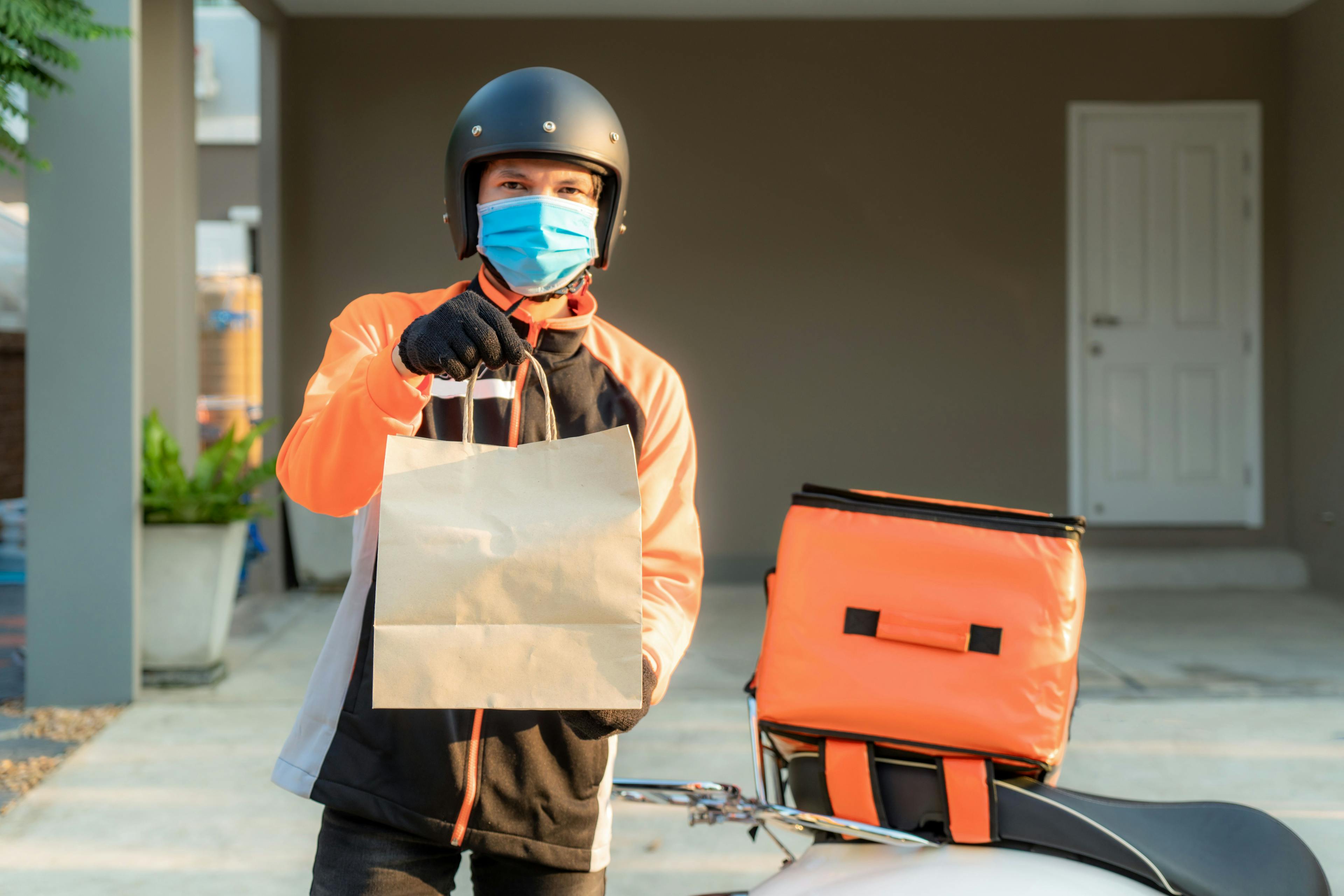 Delivery man in mask holding bag for contactless delivery platforms.