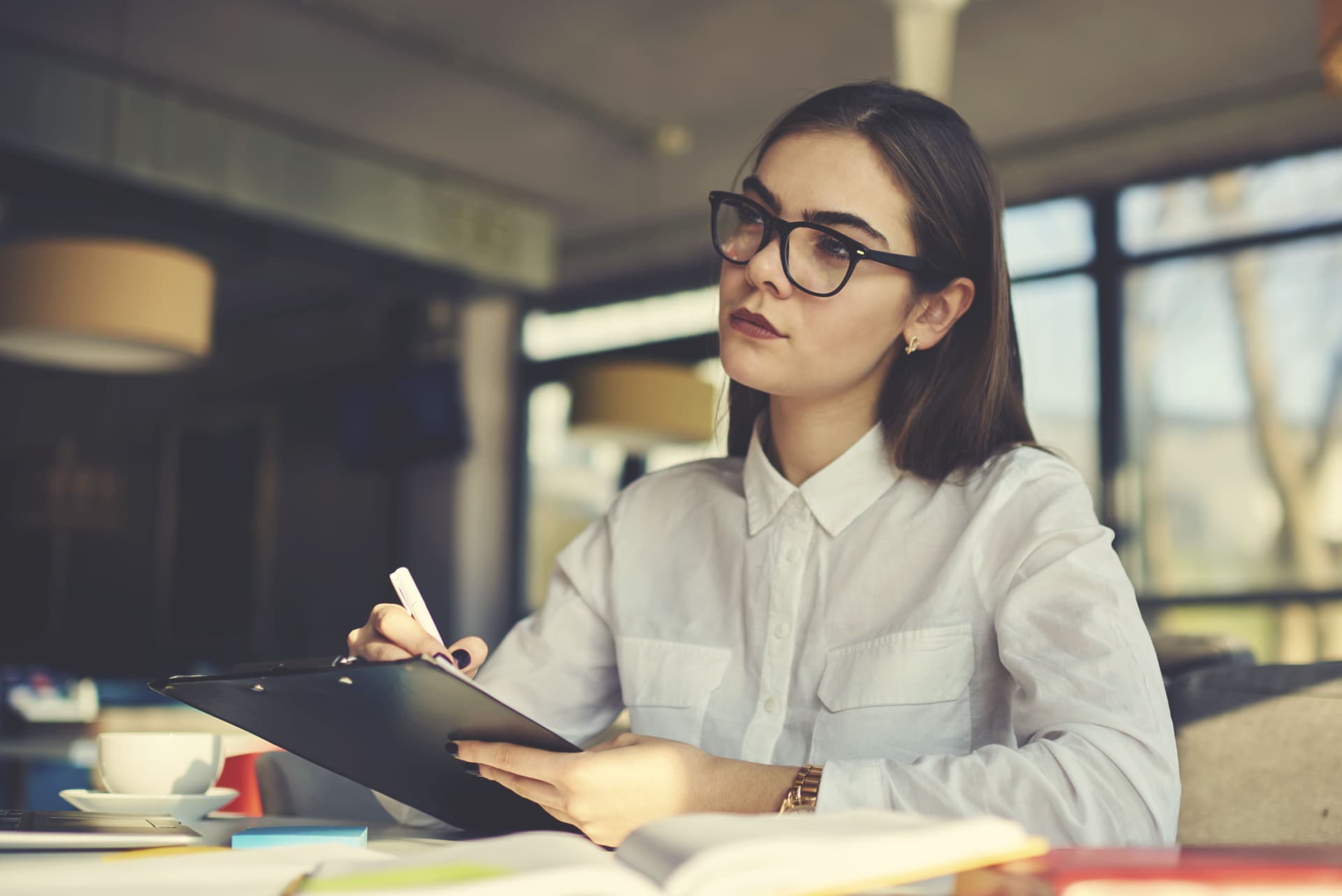 A restaurant operations manager, wearing glasses, diligently writes on a clipboard.