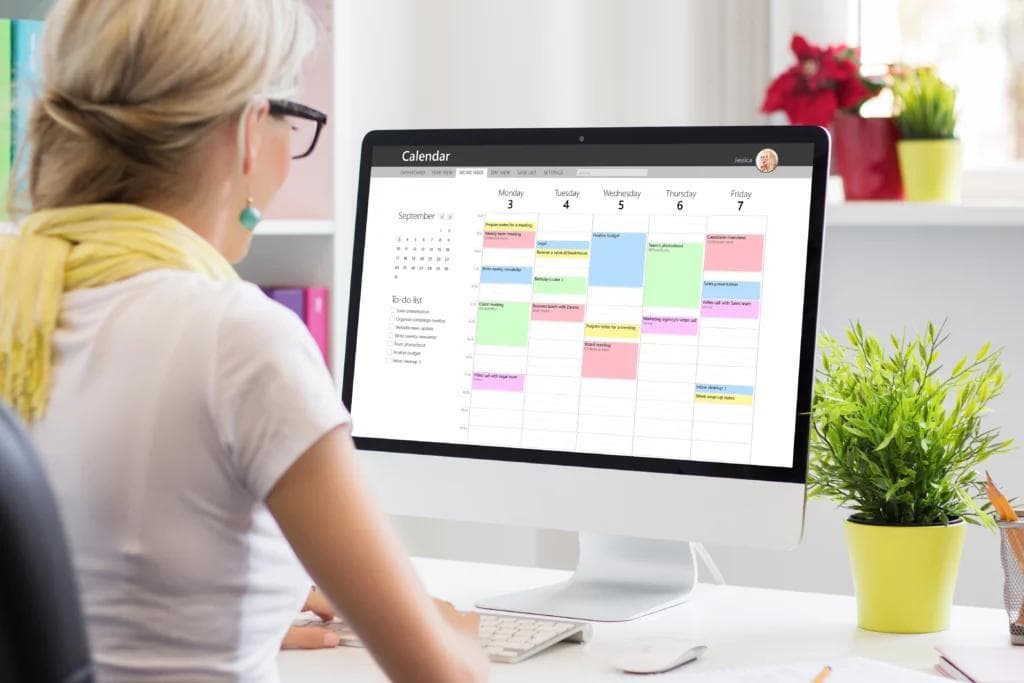 A focused woman working on her computer, with a calendar displayed on the screen.