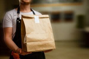 Brown paper bag held by a man for delivery and takeaway purposes.