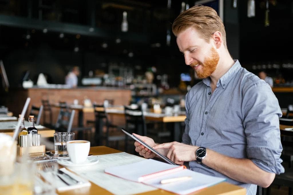 A man seated at a table, engaged with a tablet and arranging restaurant reservations.