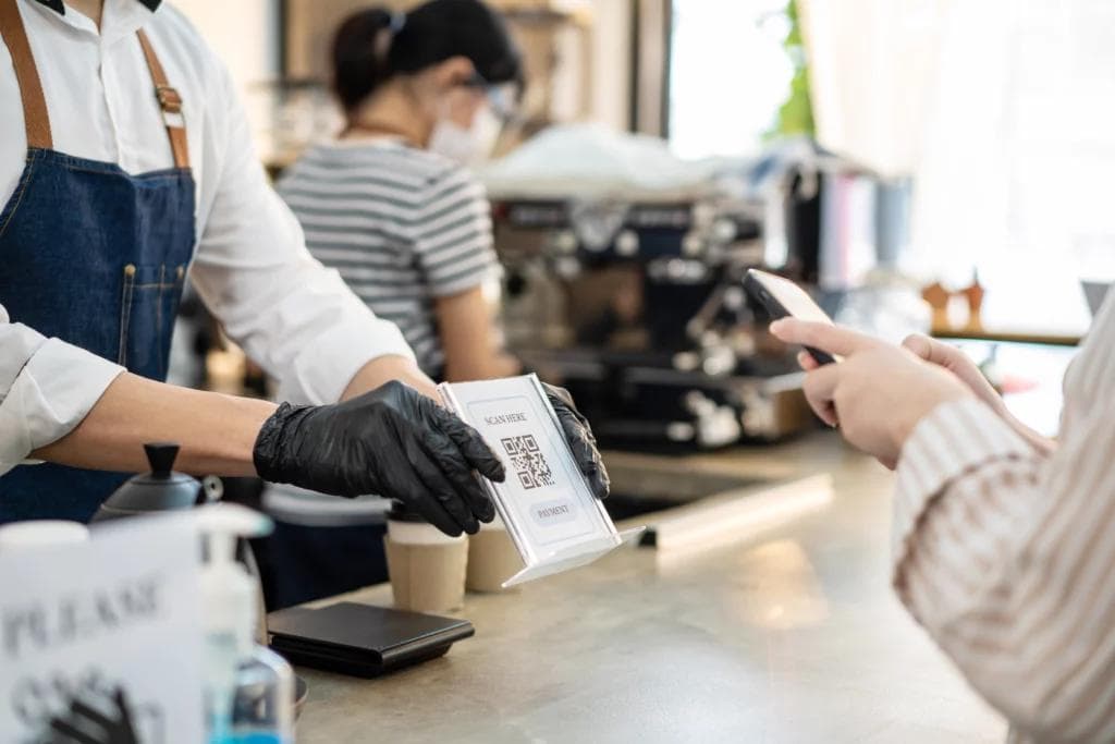 A man in an apron and gloves holds a phone while a woman holds a paper, showcasing the concept of digitizing your restaurant.