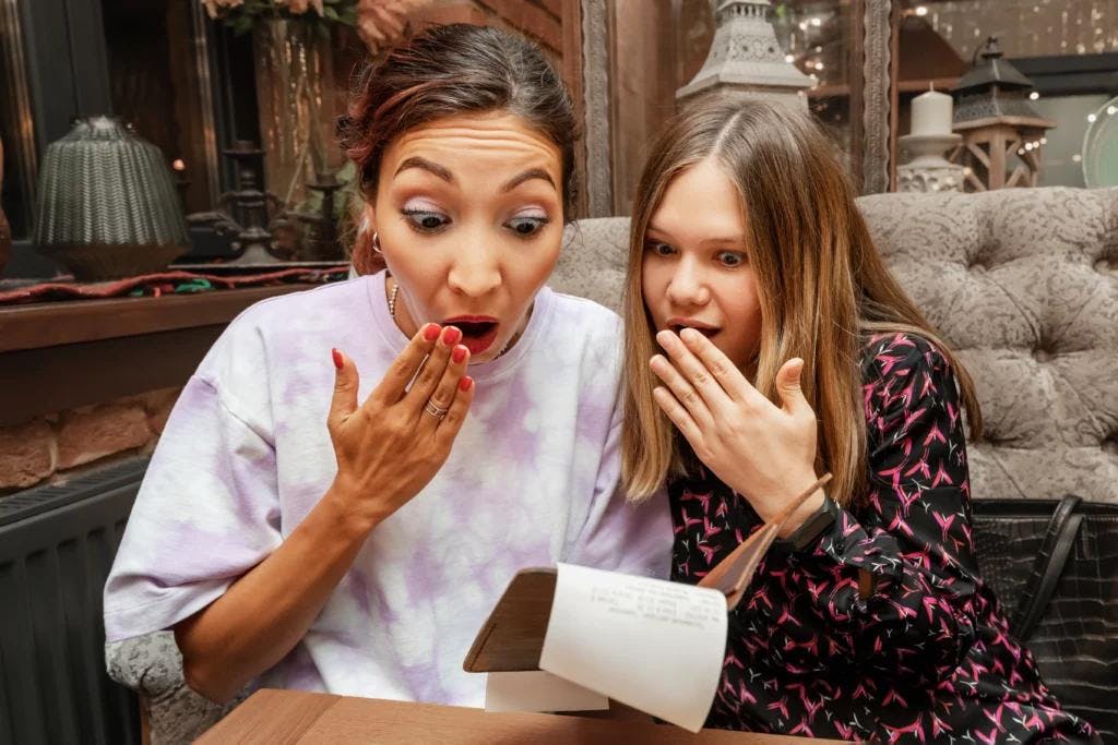 Two women examining a restaurant bill on a piece of paper.
