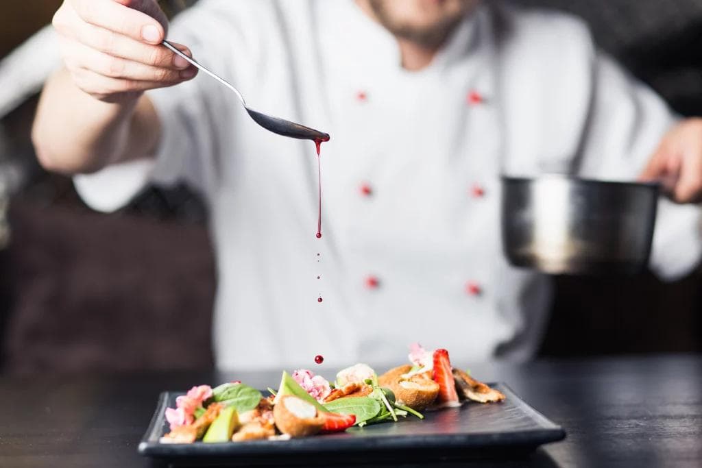 Chef prepares food on plate with sauce.