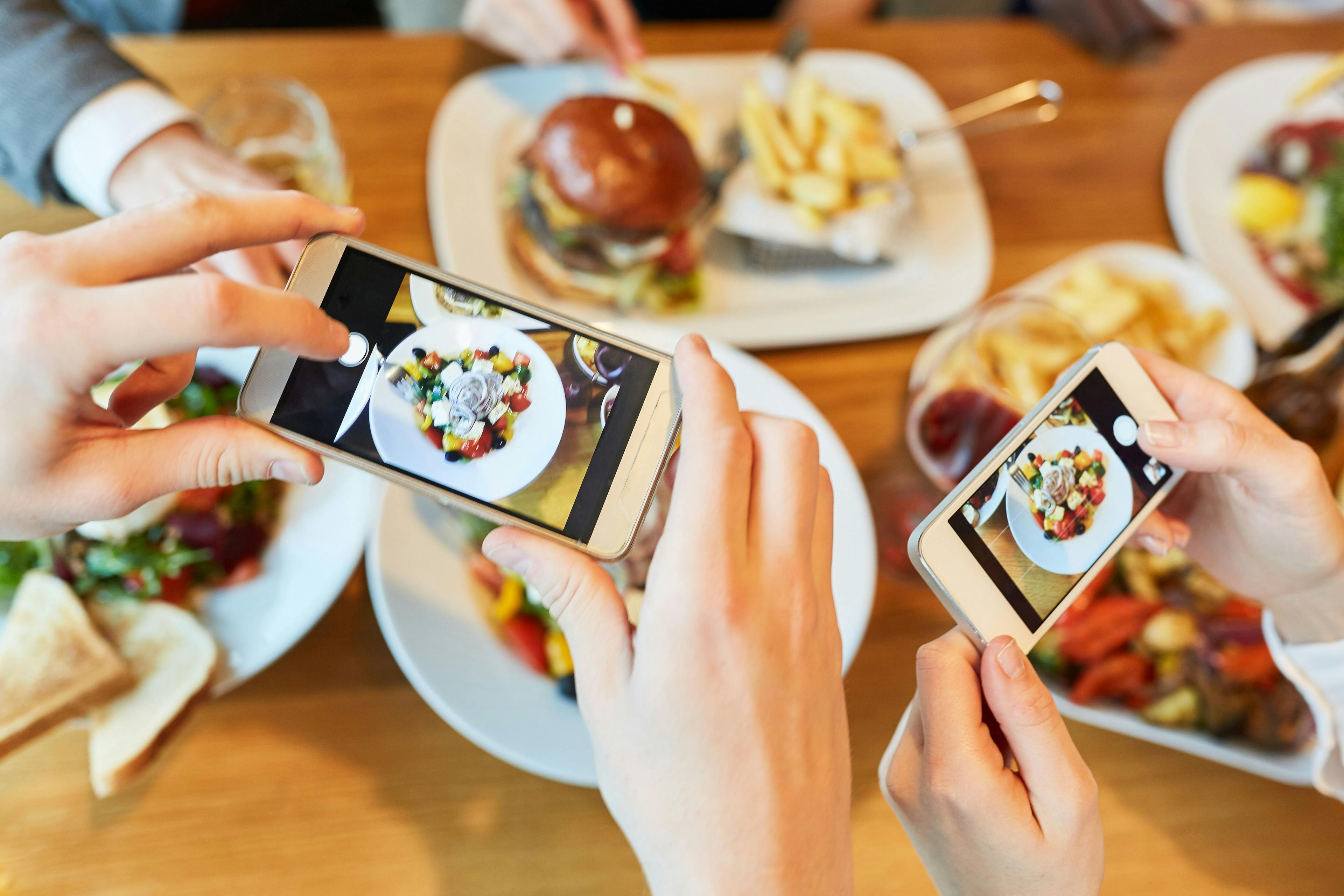 People using their phones to snap pictures of food, sharing their culinary delights on social media.