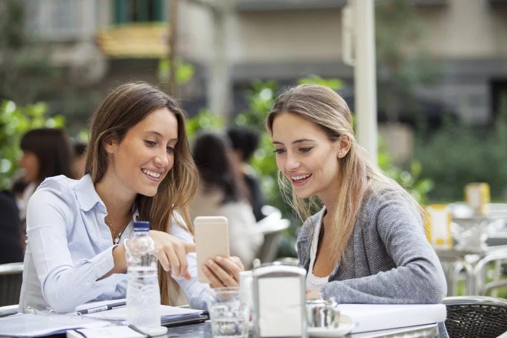 Two women at a table, looking at a cell phone using an Order & Pay app.