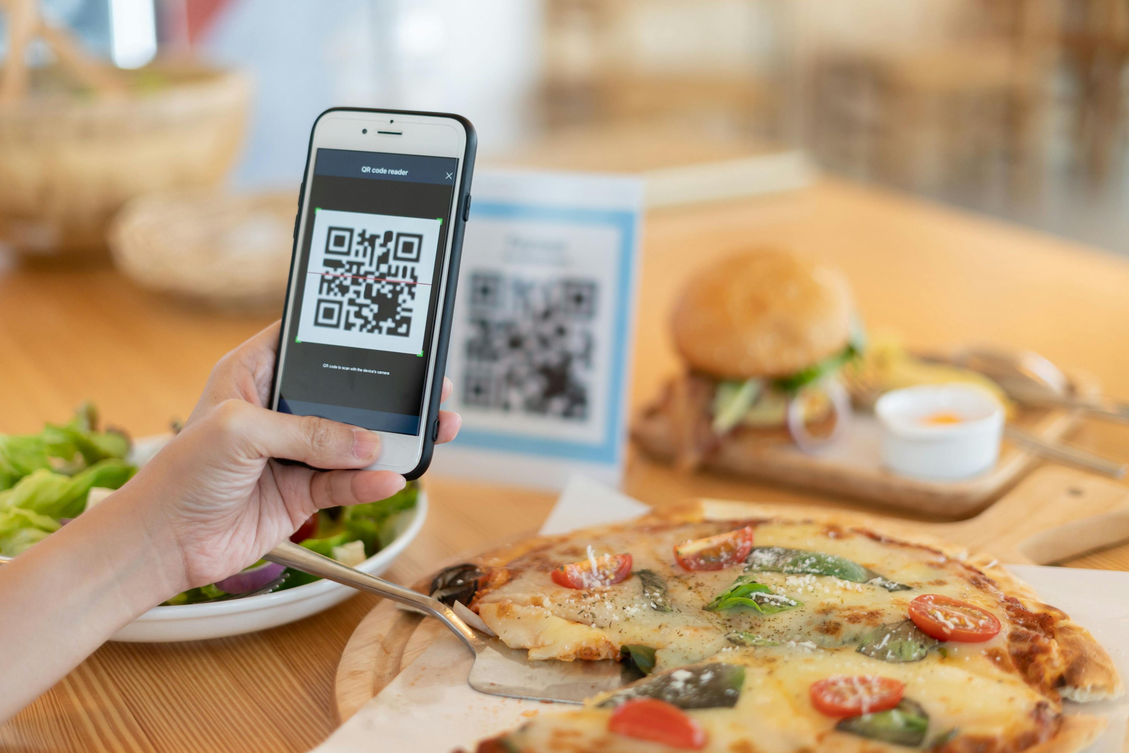 A person scans a QR code to pay for a pizza using a free QR menu.