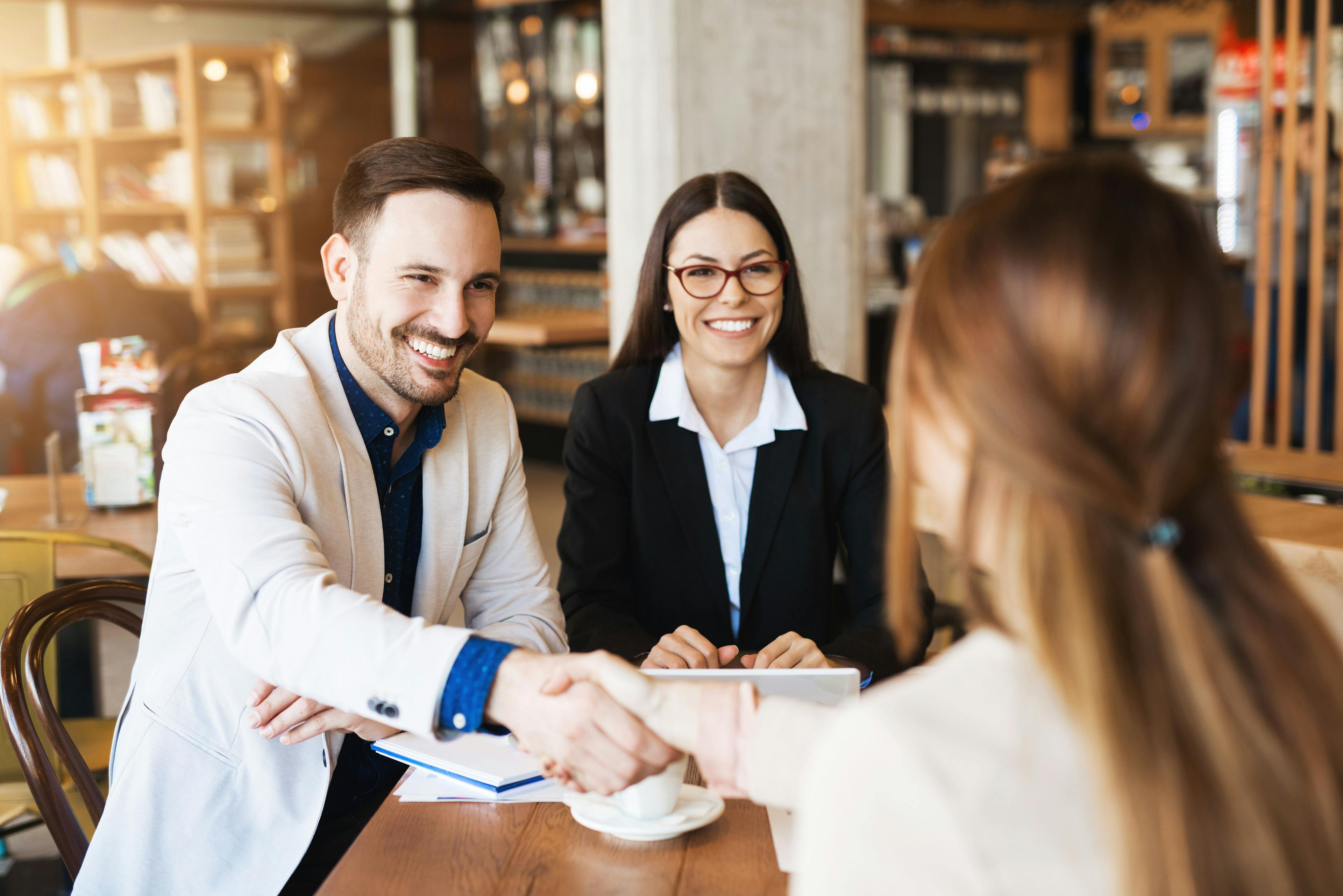 A professional man and woman seal a deal with a handshake at a table, highlighting the benefits of contactless menus.