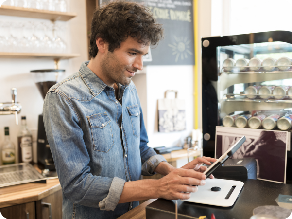 A man in a coffee shop using a tablet to seamlessly send orders from FineDine to Revel.