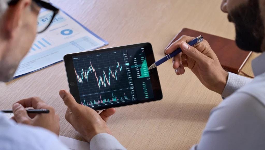 Two individuals analyzing a stock chart on a tablet, exploring dynamic pricing trends.